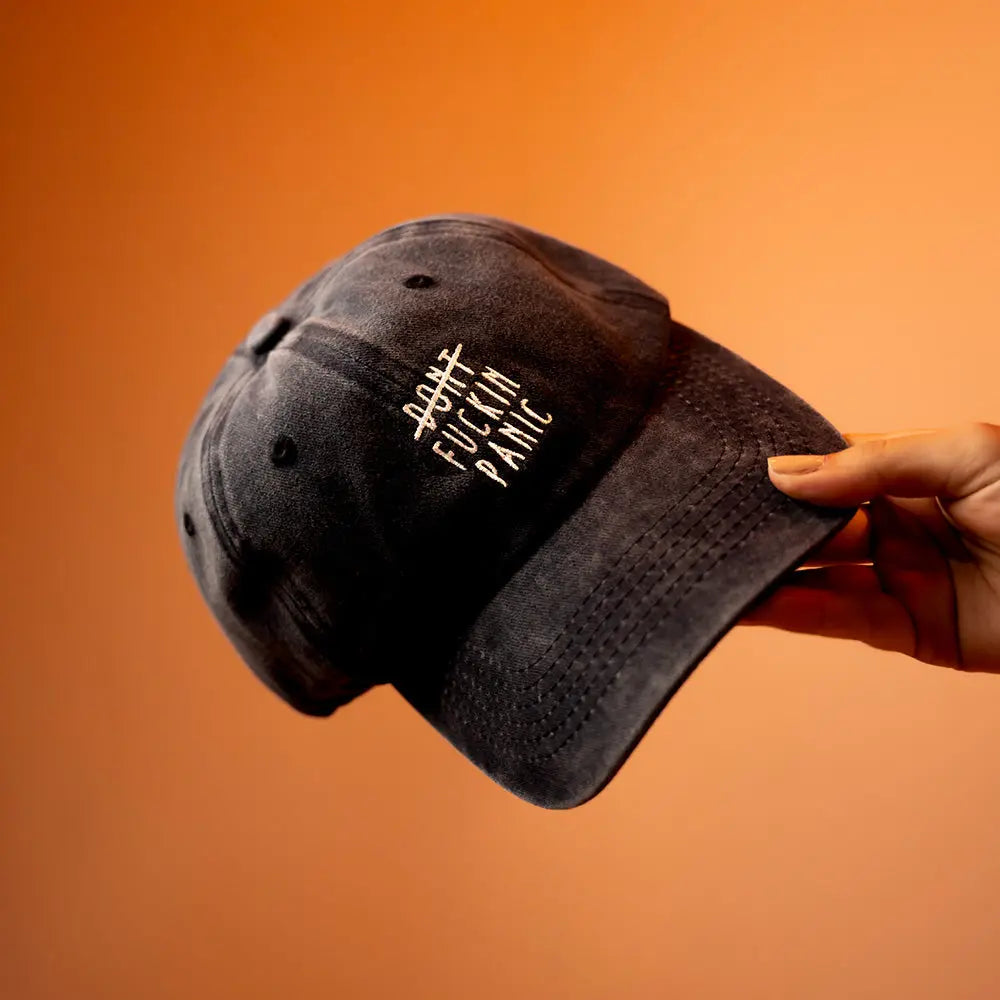 Hand holding a black Panic Zones Don't F**** Panic Cap — official Panic Zones merch